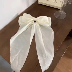 Elegant cream satin bow hair clip with long streamers on a wooden table