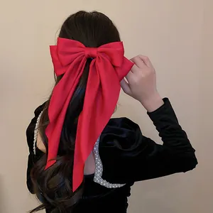 Detailed view of an elegant oversized red fabric bow hair clip on long wavy hair.