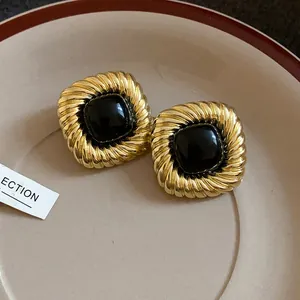 Orecchini quadrati vintage dorati a spirale con pietra nera centrale in un piatto.