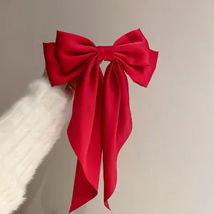 Close-up of elegant large red satin bow hair clip held against a fuzzy white sweater