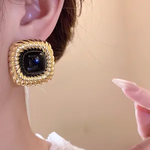 Dettaglio di orecchini vintage quadrati con trama dorata intrecciata e pietra nera