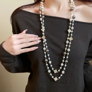 Collana lunga di perle con fiori di strass indossata su un maglione nero raffinato.
