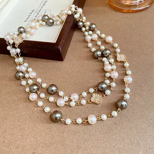 Dettaglio di una lunga collana di perle vintage multicolore con ciondoli a fiore dorati.