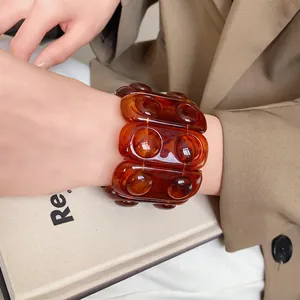 Close-up of a retro amber resin stretch bracelet worn on a wrist against a blazer and book.