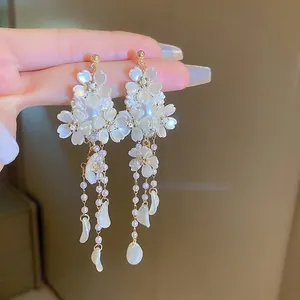 Primo piano di eleganti orecchini a fiore bianchi con lunghe nappe di perle in mano