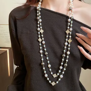 Primo piano di una lunga collana di perle con trifogli di strass su maglione marrone.