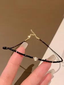 Close-up of minimalist black crystal beaded necklace with a central pearl accent.
