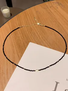 Close-up of a delicate black crystal choker necklace with gold extender on a wooden table