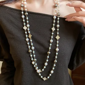 Dettaglio di una lunga collana di perle a strati con ciondoli a fiore di trifoglio diamantati