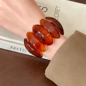 Close-up view of a chunky amber-colored oval elastic bracelet worn on a female wrist