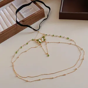 Detailed view of an enamel butterfly thigh chain with green stones and gold metal finish.