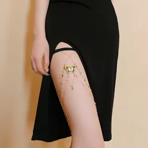Detail view of a green butterfly enamel thigh chain worn on a leg with a black dress