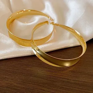 Elegante goldene Metall-Creolen mit Hochglanz-Spiegelfinish auf Seide und Holz