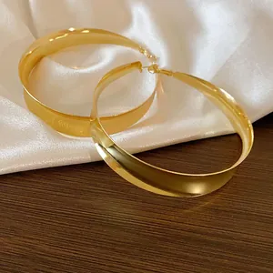 Detailaufnahme von übergroßen metallischen Creolen mit Goldfinish auf Seidenhintergrund