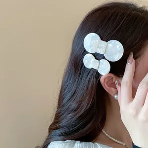 Detail of elegant white marbled resin bow hair clips worn on side hair for women.