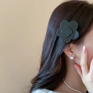 Close-up of minimalist black resin flower hair clip worn by a model on dark hair