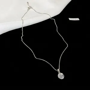 Minimalist silver necklace with round translucent resin pendant on black and white background.