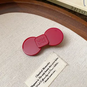 Close-up of a minimalist red resin duckbill hair clip on a textured fabric background.