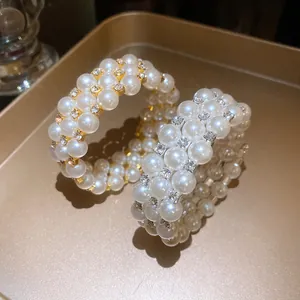 Detailed close-up of three-layer faux pearl and rhinestone open bangle in gold finish