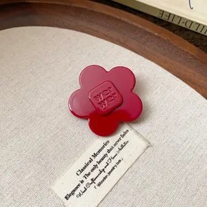 Close-up of a red resin flower hair clip with embossed text on a vintage display board