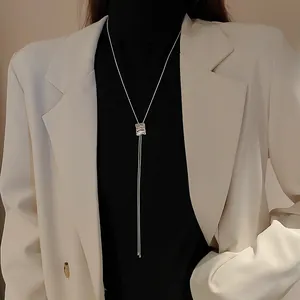 Gros plan d'un long collier pull argenté porté sur un col roulé noir et un blazer blanc.