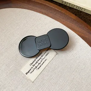 Minimalist black resin hair clip with an elegant bowtie design on a rustic wooden tray