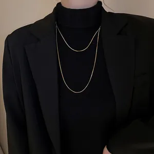 Collier double chaîne serpent dorée sur pull à col roulé noir et veste blazer.