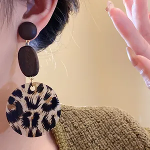 Macro view of leopard print round wooden drop earrings worn by an elegant model