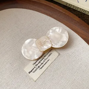 Close-up of elegant cream resin hair clip with embossed detail on fabric background