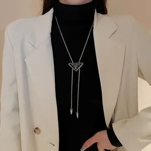 Détail d'un collier pendentif triangulaire argenté sur col roulé noir et blazer blanc.