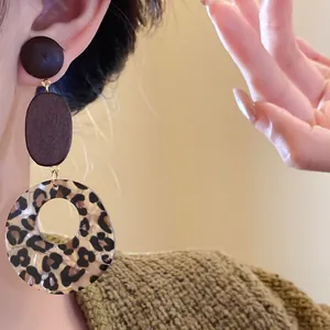 Close-up view of elegant Bohemian leopard print and wood dangle earrings on an Asian model