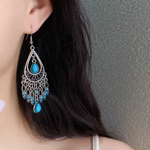 Detail view of bohemian tassel earrings with turquoise drops and blue rhinestones on a model.