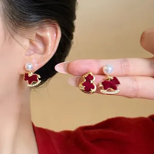 Vue détaillée de boucles d'oreilles dorées avec perles et cheval à bascule en velours rouge.