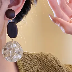 Close-up of elegant wooden dangle earrings featuring a shell pattern resin pendant
