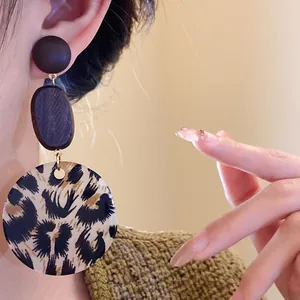 Close-up of leopard print drop earrings with wooden studs and textured fabric background.