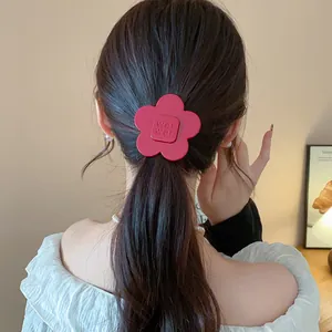 Detail of a minimalist red resin flower hair clip styled on a woman's low ponytail