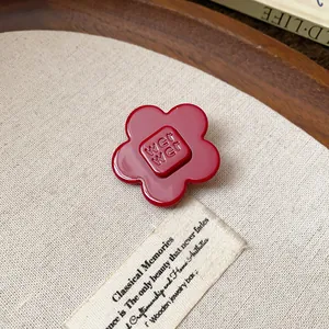 Detail of a red resin flower hair clip with square embossed center on a fabric background