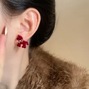 Gros plan d'une boucle d'oreille cheval en velours rouge avec nœud doré et perle