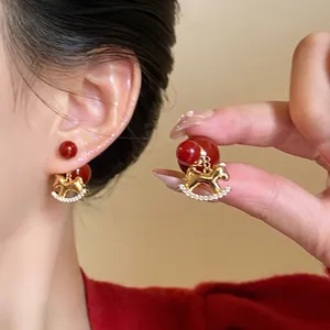 Vue détaillée de boucles d'oreilles cheval à bascule dorées et perles rouges sur un modèle