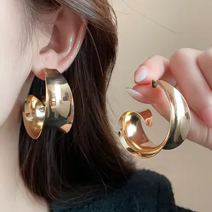 Close-up of oversized wide golden metal earrings with curved minimalist design