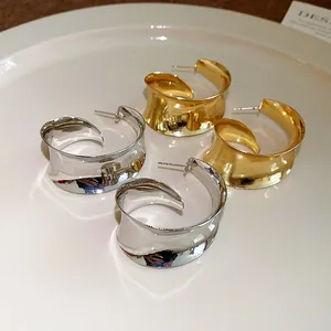 Close-up of gold and silver wide metal hoop earrings with irregular wavy design