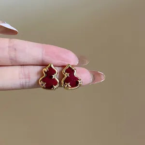 Vue détaillée des boucles d'oreilles gourde dorées avec velours rouge et étoiles dorées.