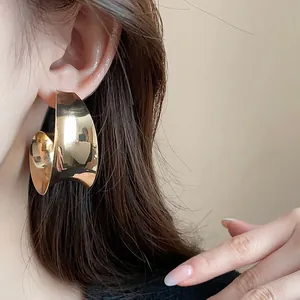 Detailed view of model wearing high-end wide-faced metallic gold exaggerated earrings