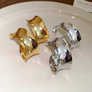 Detail view of chunky wide-surface metal hoop earrings in gold and silver finish