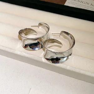 Close-up of minimalist silver wide metallic C-shaped hoop earrings on display tray