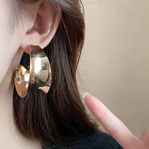 Close-up detail showing the metallic texture of an oversized gold wide-surface stud earring