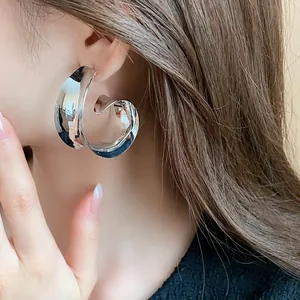 Close-up view of a large silver metallic swirl earring worn by a model.