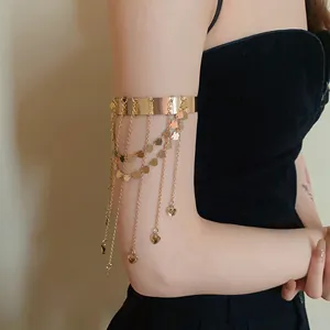 Gouden bovenarmband met hartvormige kwastjeskettingen om de arm
