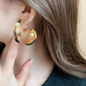 Close-up detail of a minimalist oversized gold metallic spiral earring worn by a model
