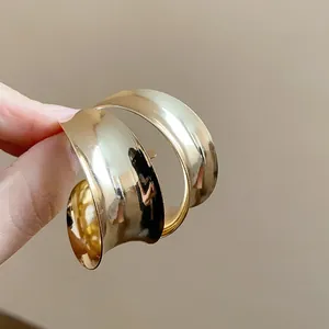 Detailed macro shot of wide gold C-shaped metal hoop earrings with a smooth glossy finish.